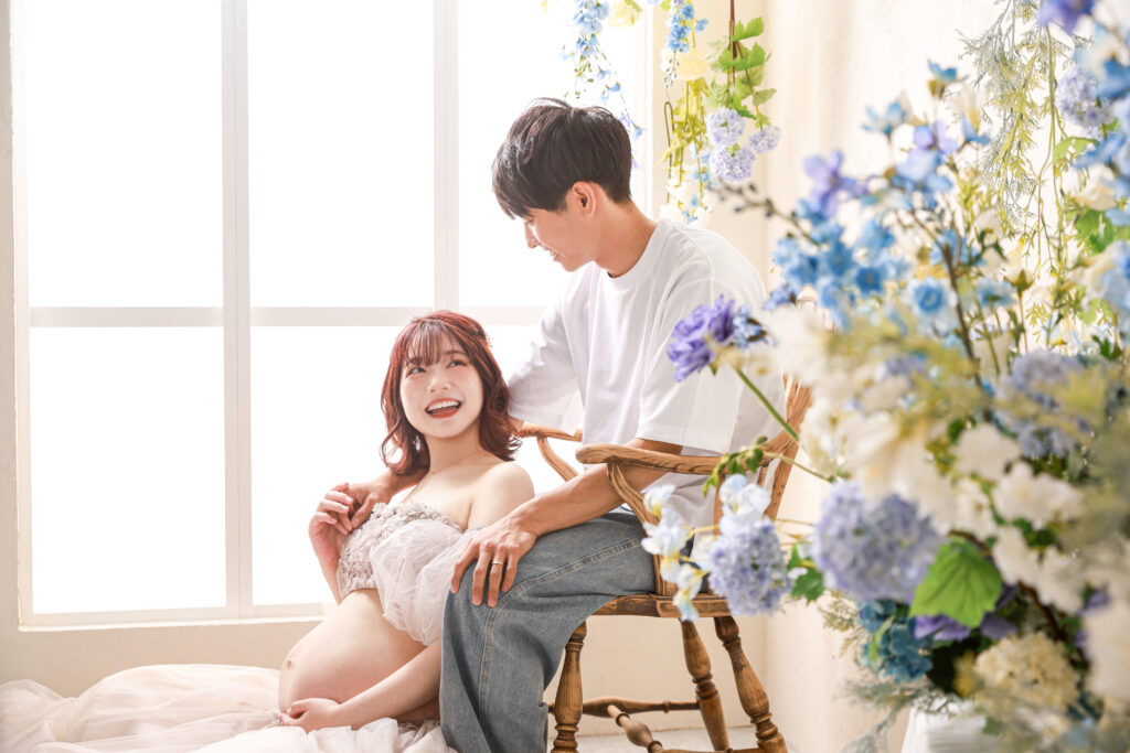 花があふれるスタジオで妊娠中のママとパパが見つめあうマタニティフォト